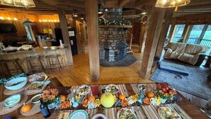 A rustic dining area with a stone fireplace, wooden beams, and a large table set for a meal. - UNFORGETTABLE TIMES...500+ ACRES, 3/4 MILE ON PINE CREEK! (Gaines)