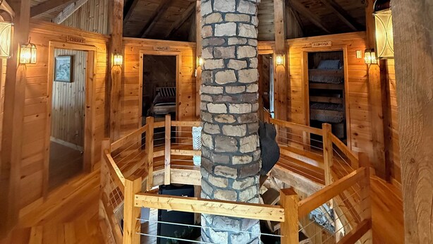 A wooden cabin interior with a stone fireplace, wooden beams, and a spiral staircase. - UNFORGETTABLE TIMES...500+ ACRES, 3/4 MILE ON PINE CREEK! (Gaines)
