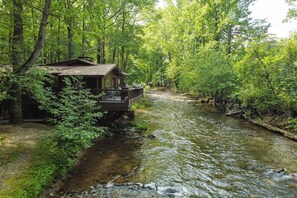 Une cabane dotée d’une terrasse donnant sur une rivière, entourée d’une forêt dense.