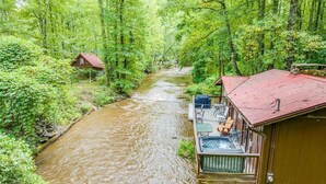 A cabin with a hot tub and deck overlooking a river. - River's Edge - Ultimate Riverfront Cabin w/Hot Tub (Helen)