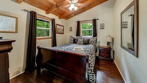 A bedroom with a wooden ceiling, a bed, a nightstand, a mirror, and a window. - River's Edge - Ultimate Riverfront Cabin w/Hot Tub (Helen)