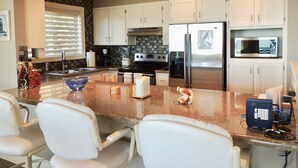 A modern kitchen with white cabinets, stainless steel appliances, a granite countertop, and a seating area with white chairs. - Toby's Crab Shack, Oceanside in Brookings, Oregon (Brookings)