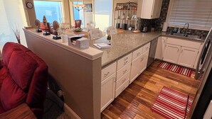 A modern kitchen with a central island, white cabinetry, and a view of the ocean. - Toby's Crab Shack, Oceanside in Brookings, Oregon (Brookings)