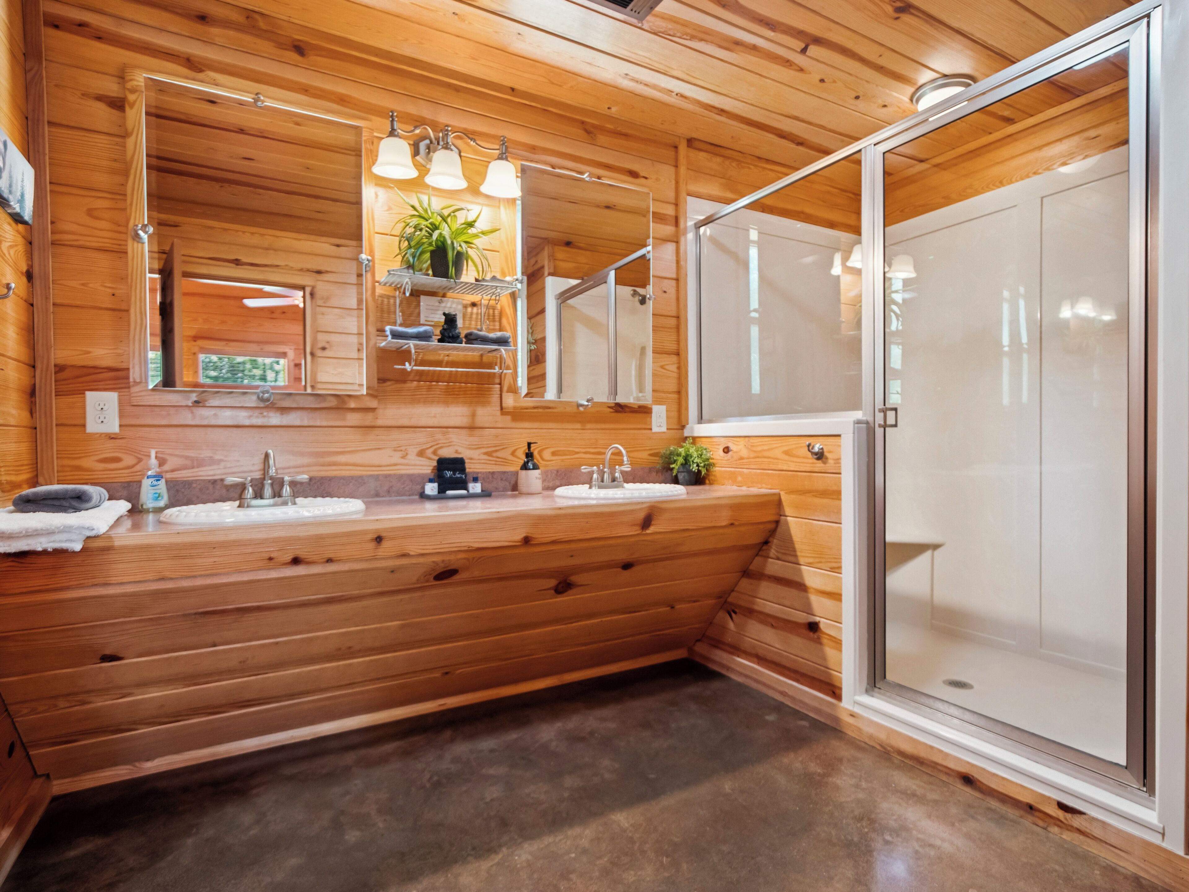 A wooden cabin-style bathroom with a large sink, mirror, and shower area.