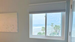 A room with a window overlooking a beach, palm trees, and a clear sky. - Oceanfront Condo • 2026 Renovations! • 2 BD, 2BA (Myrtle Beach)