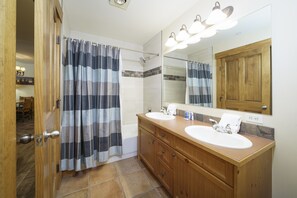 Een badkamer met een houten wastafelmeubel, twee wastafels, een douche met gestreepte gordijnen en een grote spiegel.