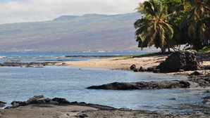 Une plage bordée d’une côte rocheuse, avec des palmiers et des montagnes qui se dessinent à l’horizon.