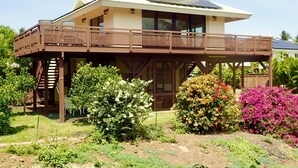 Une maison à deux étages dotée d’un balcon, entourée d’un jardin où poussent différentes plantes et fleurs.
