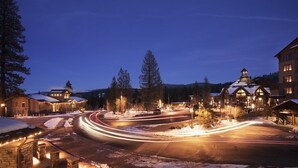 A snow-covered street at dusk with illuminated buildings and a clear sky.