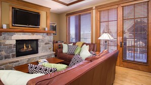 A living room with a stone fireplace, a leather sofa, and a television mounted above it.