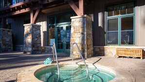 An outdoor hot tub area with stone pillars, a wooden bench, and a metal ladder.