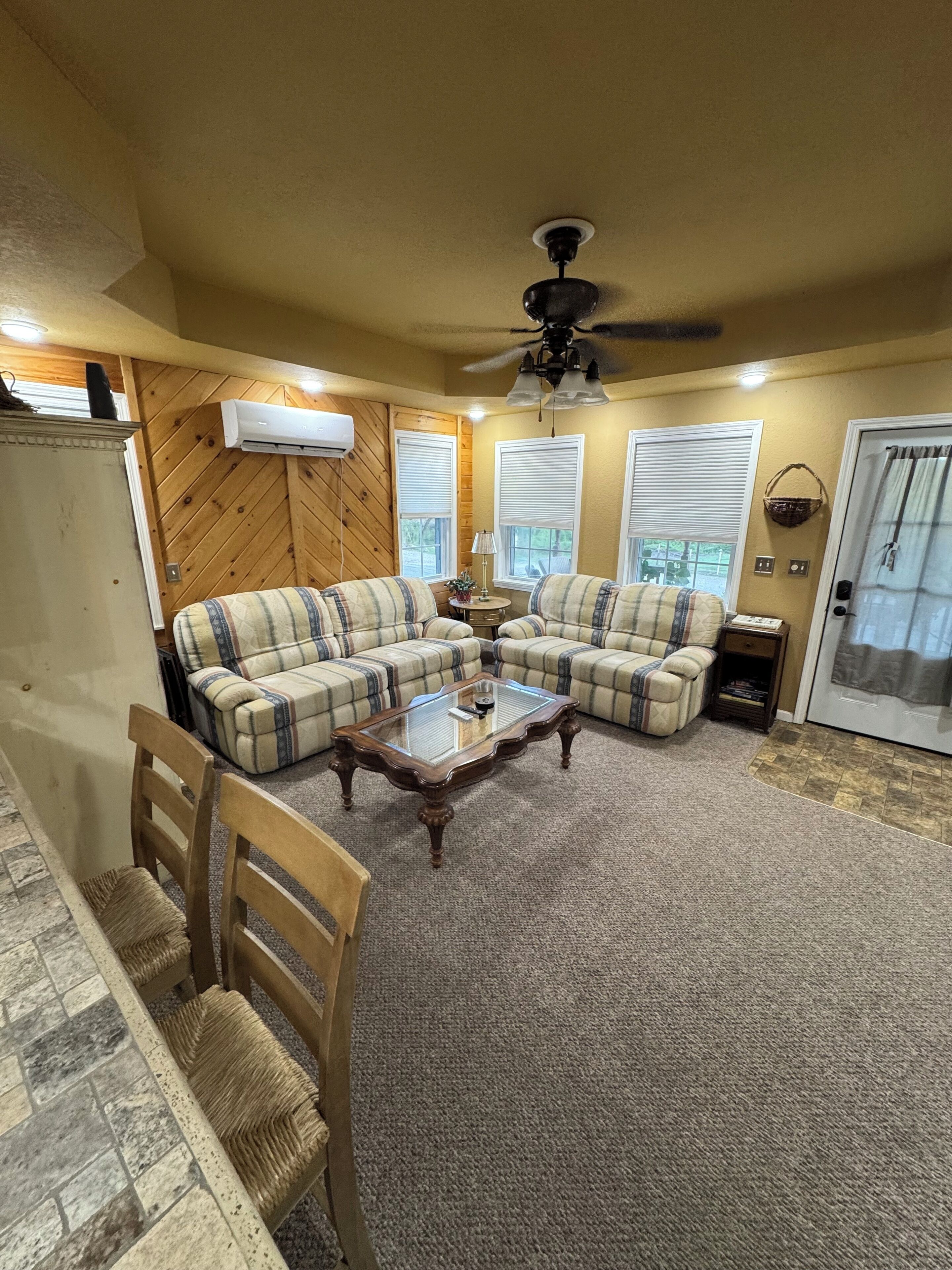 A living room with a sectional sofa, a glass coffee table, a ceiling fan, and a door with a curtain.