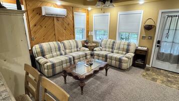 A living room with a sectional sofa, a glass coffee table, a ceiling fan, and a door with a curtain.