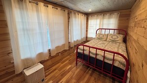 A wooden-paneled room with a bed, curtains, and a heater.