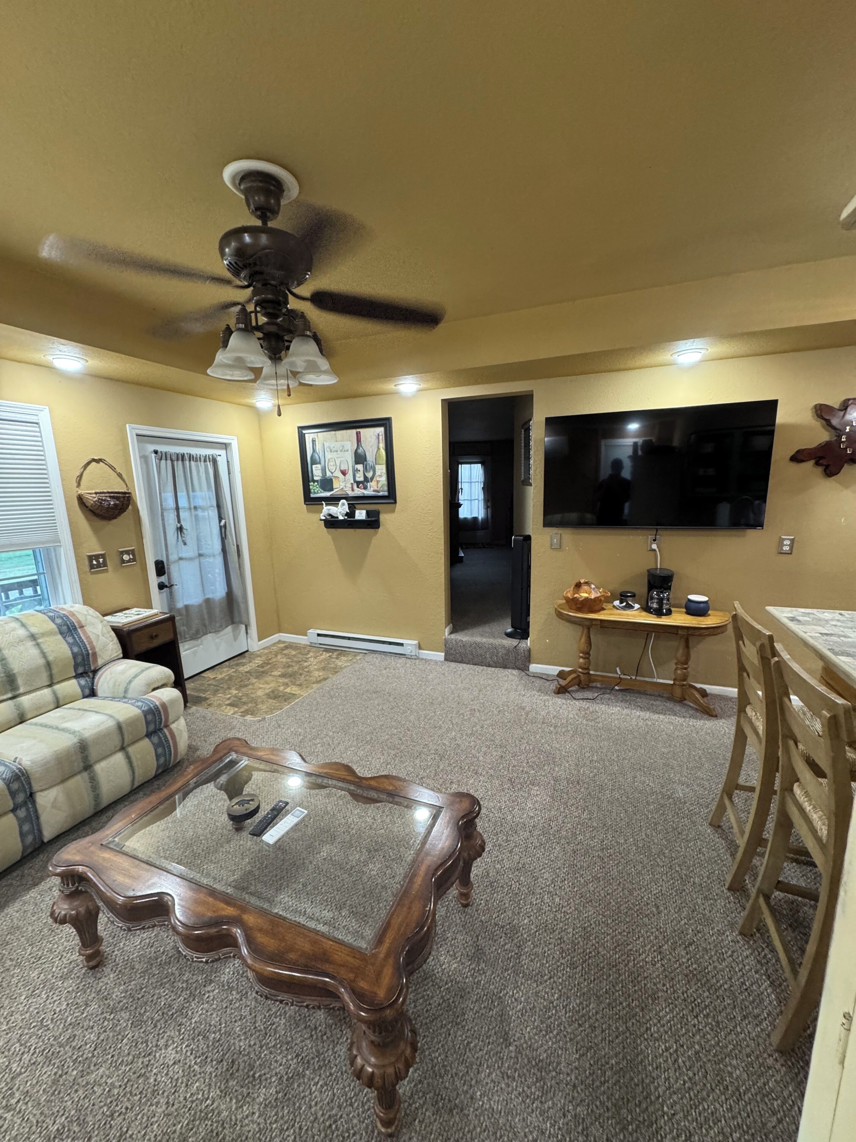 A living room with a ceiling fan, a television, a coffee table, a sofa, and a dining area with chairs.