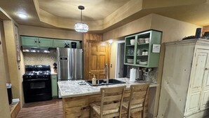 A kitchen with wooden cabinets, a stainless steel refrigerator, a wooden island with bar stools, and a chandelier.