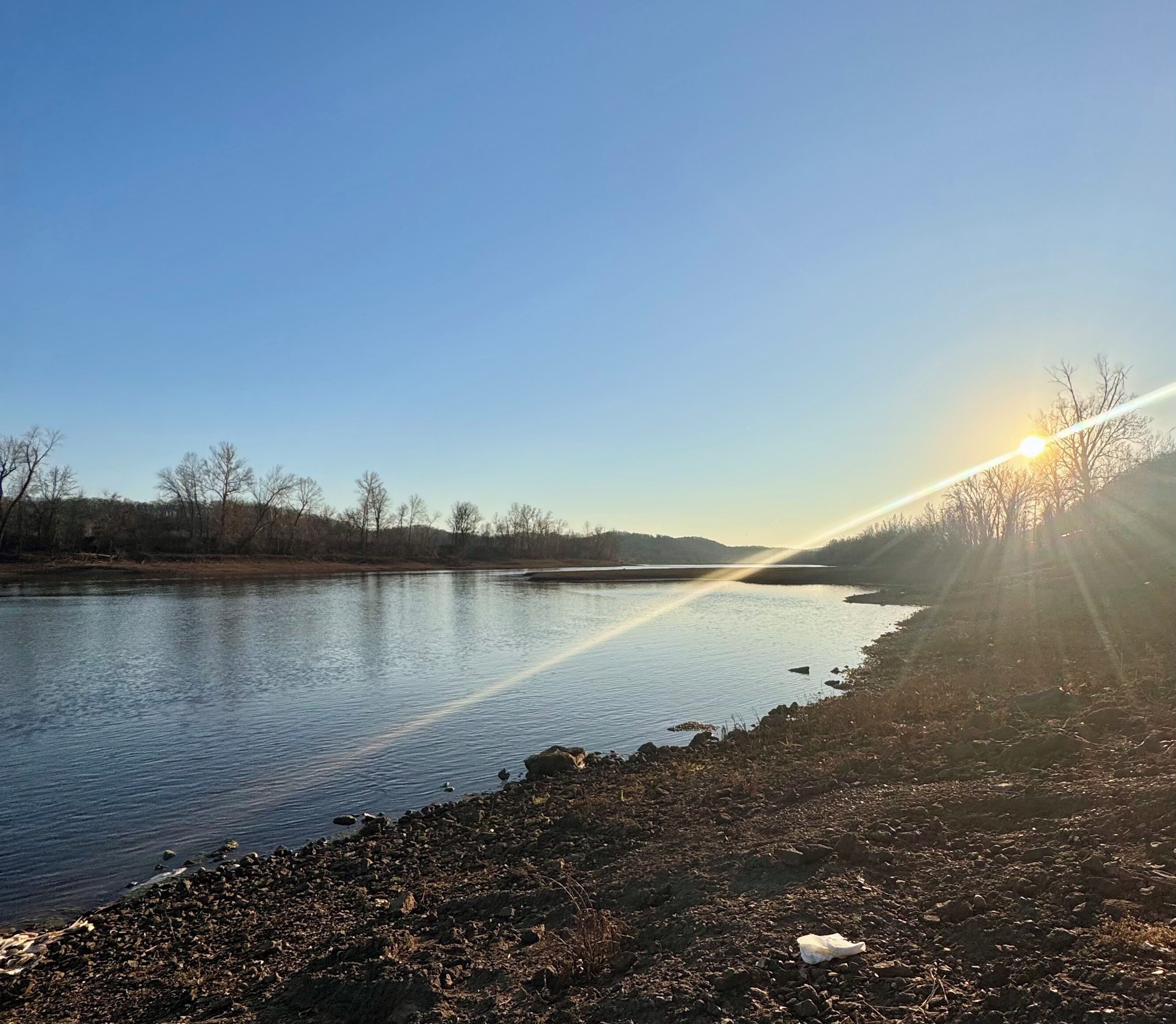 Une rivière aux eaux claires, sous un ciel dégagé, où la lumière du soleil se reflète.