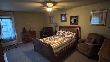 A bedroom with a bed, a chair, a desk, a ceiling fan, and framed pictures on the wall.