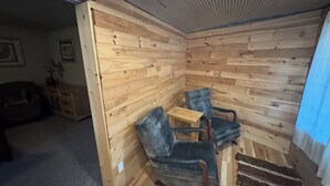 A room with wooden panel walls, a small wooden table, two chairs, a rug, and a doorway leading to another room.