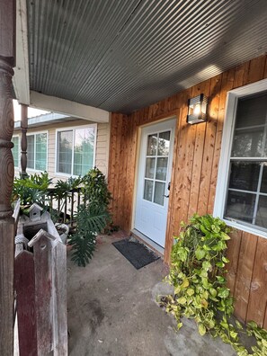 A wooden exterior with a white door, a small porch area, and a birdhouse. - Great Cabin on Osage River in Tuscumbia, MO (Tuscumbia)
