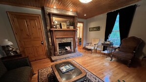 A cozy living room with a stone fireplace, wooden furniture, and a large window with curtains. - LOCATED IN ABINGDON, VA - PRIVATE, TRANQUIL SETTING (Abingdon)