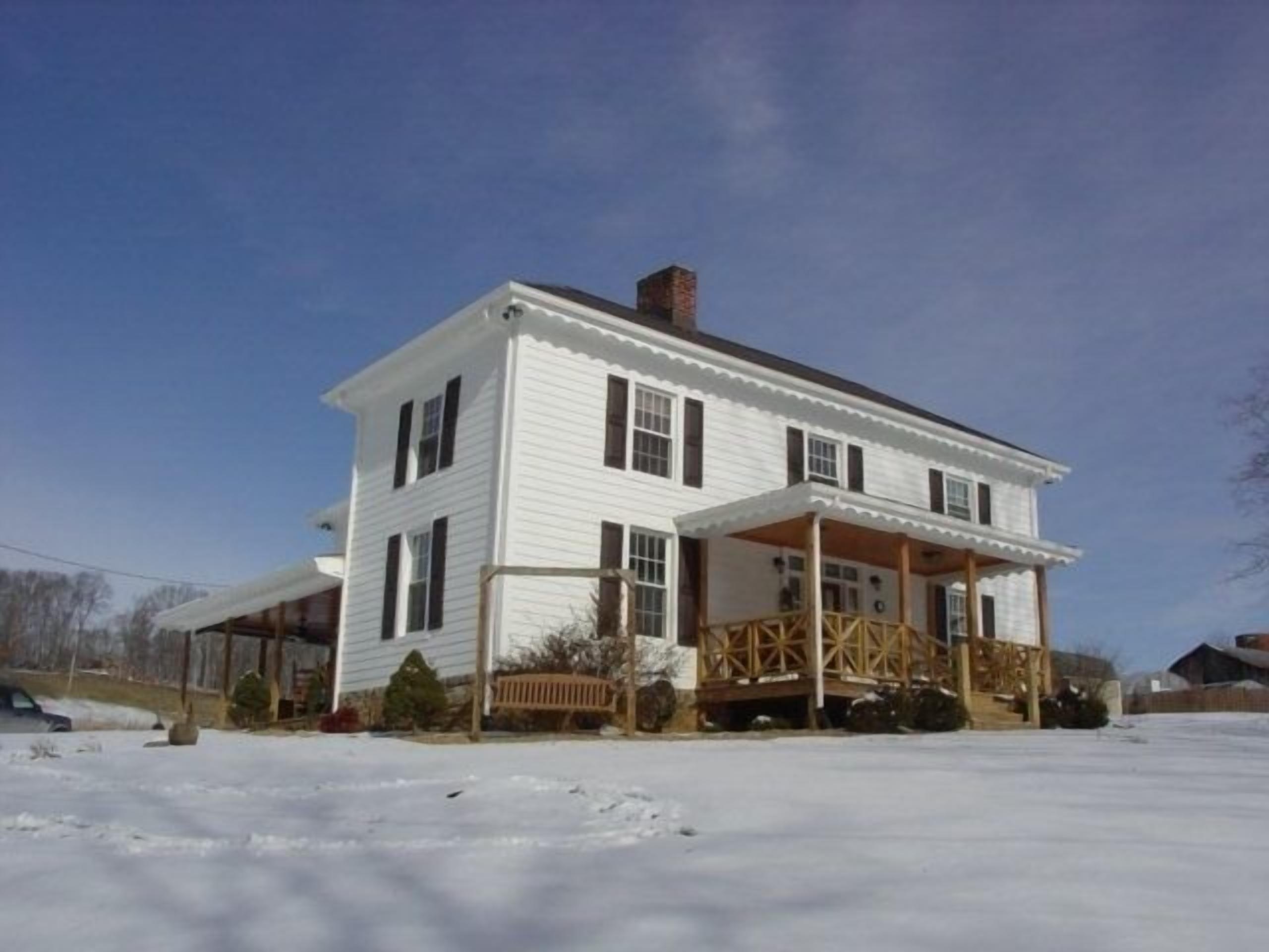 Une maison blanche à deux étages, dotée d’un porche et d’une cheminée.