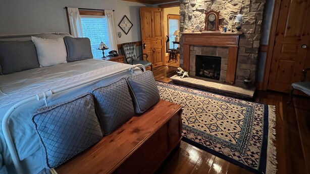 A bedroom with a large bed, wooden headboard, a stone fireplace, and a wooden bench. - LOCATED IN ABINGDON, VA - PRIVATE, TRANQUIL SETTING (Abingdon)