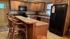 A kitchen with wooden cabinets, a black refrigerator, a microwave, and a bar area with wicker chairs. - LOCATED IN ABINGDON, VA - PRIVATE, TRANQUIL SETTING (Abingdon)