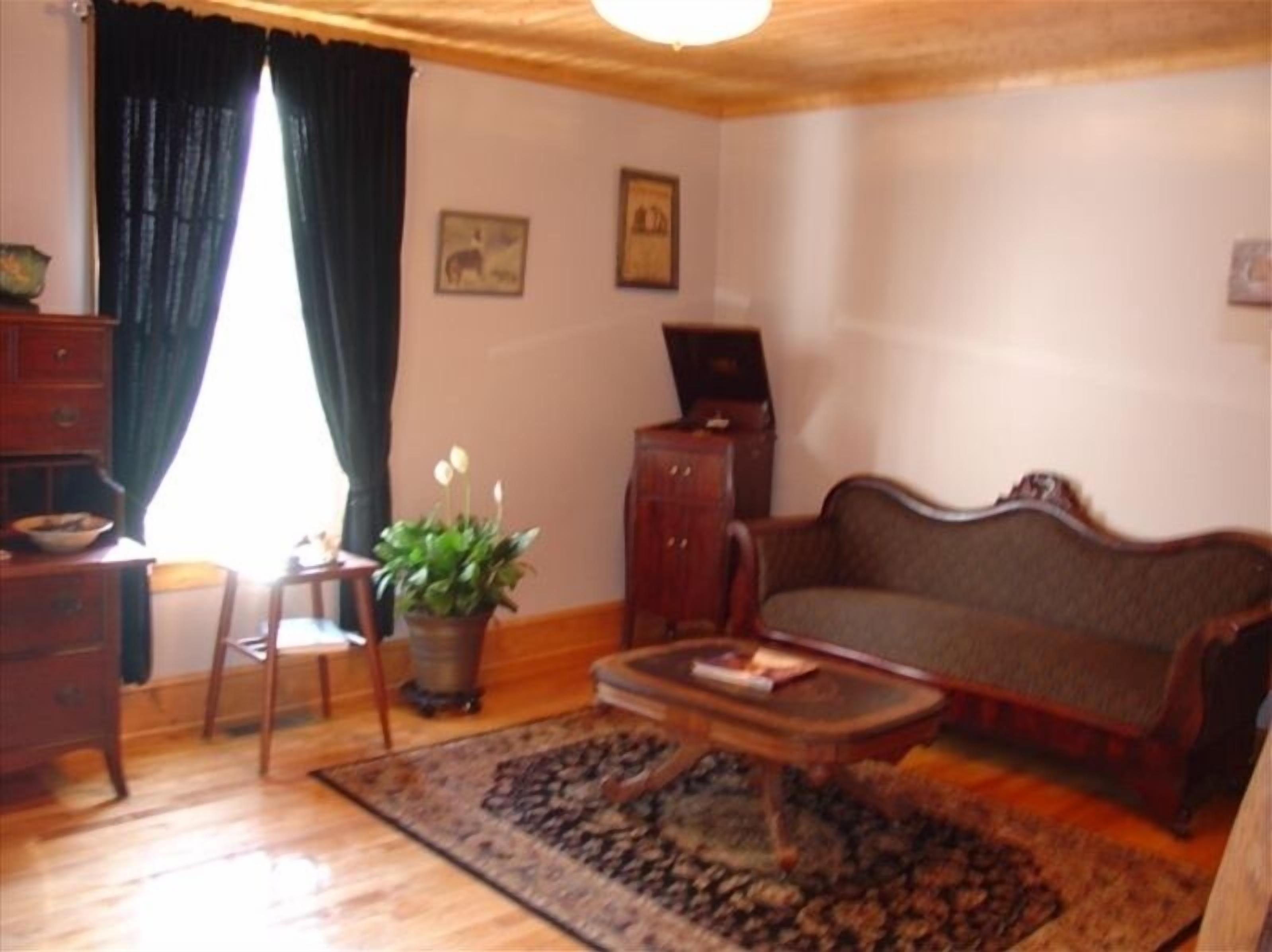 A living room with a wooden floor, a sofa, a coffee table, a potted plant, a chair, a cabinet, and a window with curtains.