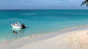 En strand med kristallklart, turkosfärgat vatten, en båt som ligger ankrad nära stranden och ett palmträd i förgrunden.