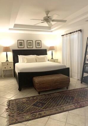 A neatly arranged bedroom with a large bed, two bedside tables with lamps, a ceiling fan, and a patterned rug. - The Best of Everything in Providenciales, Part II (Providenciales)