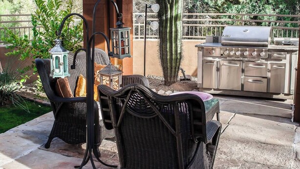 Een terras buiten met rieten meubilair, een barbecue en een cactus.