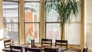 Een eethoek met een houten tafel en stoelen, een plant en een raam met jaloezieën.