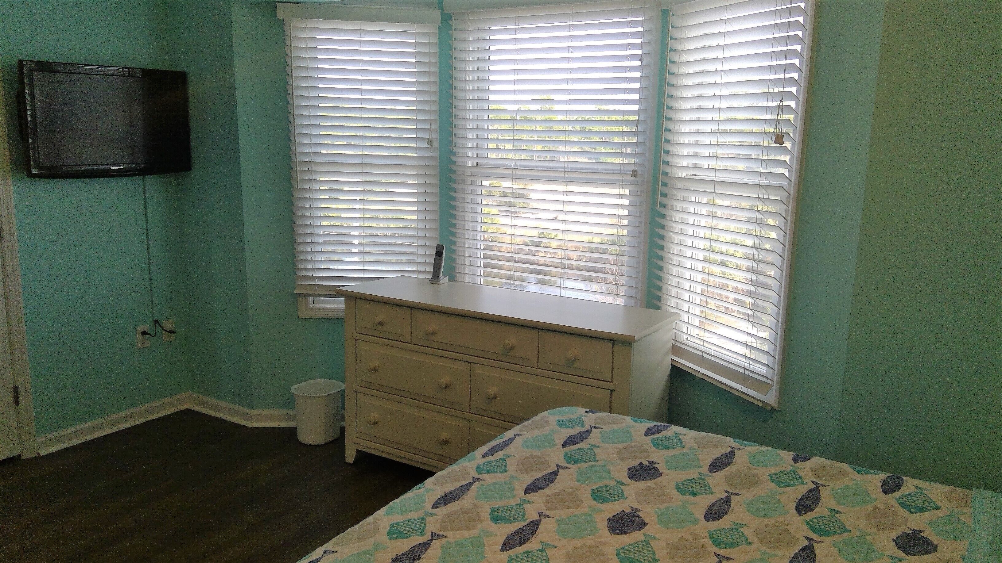 A bedroom with a bed, a dresser, and a window with blinds.