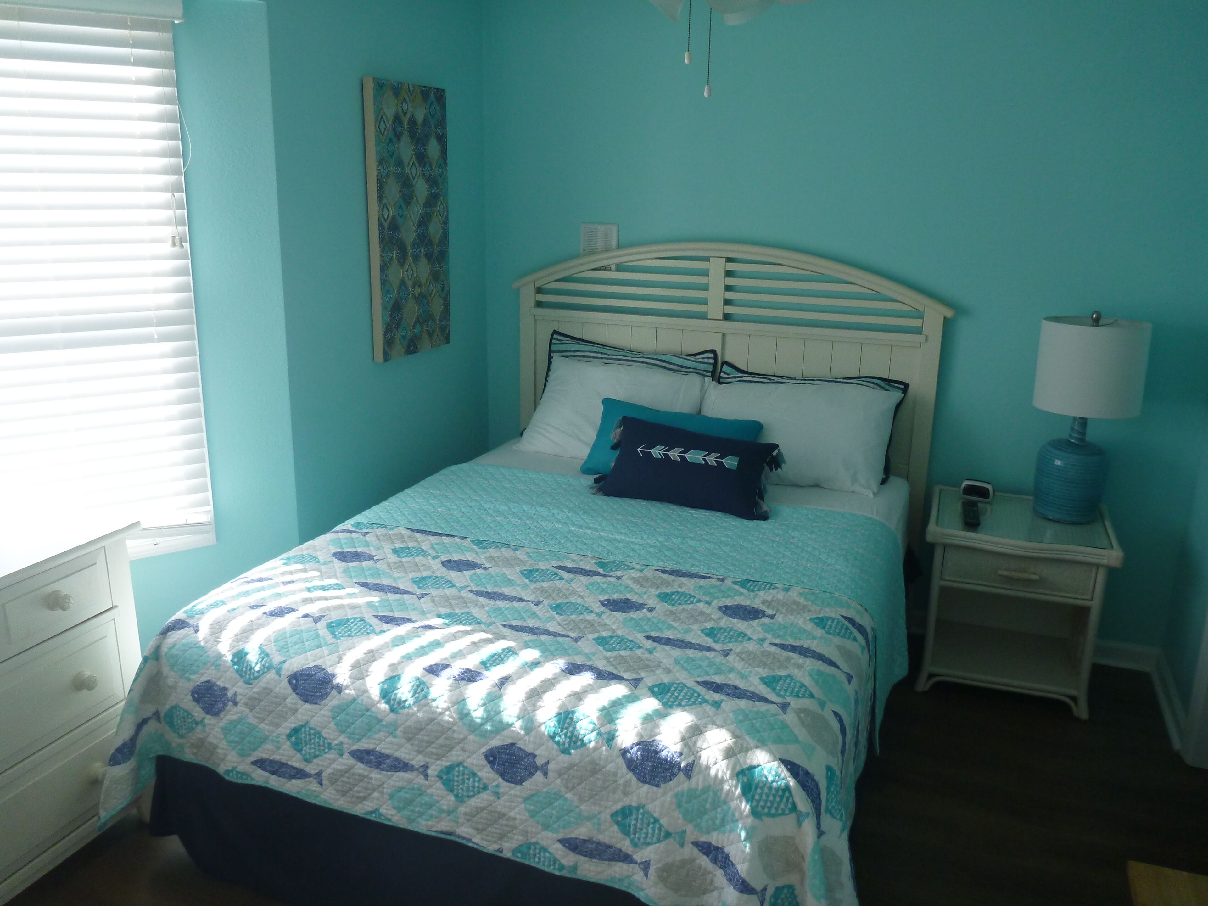 A bedroom with a bed, a nightstand, a lamp, and a window with blinds.