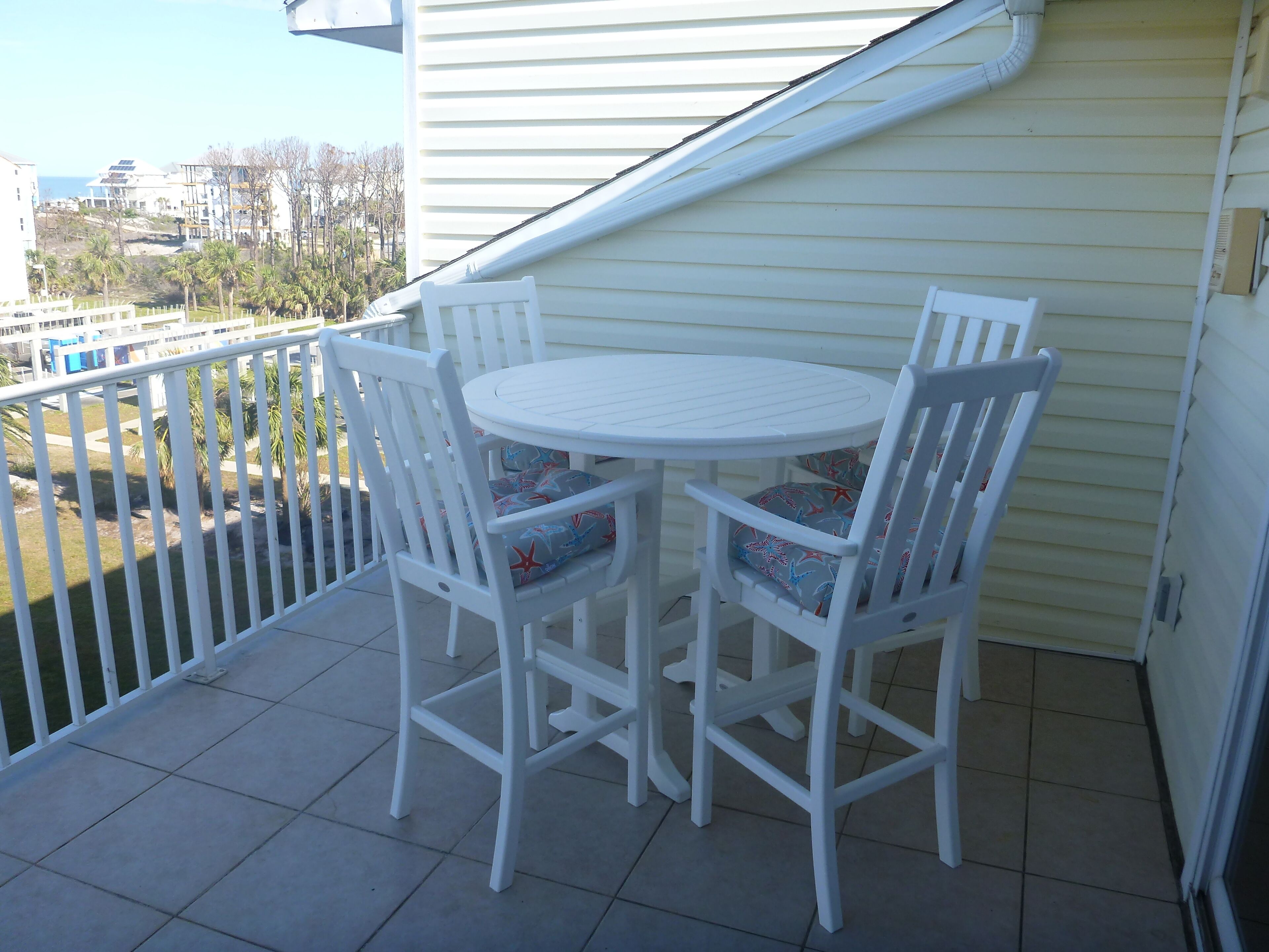 Un balcon avec une table et des chaises blanches, un sol carrelé et une vue sur les environs.