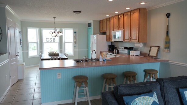 A kitchen with a central island, wooden cabinets, a chandelier, and a view of the outside through large windows. - Gulf View 4/4.5-Seacliffs /dog friendly/community pool/ steps to beach-SPECIALS! (Port St Joe)