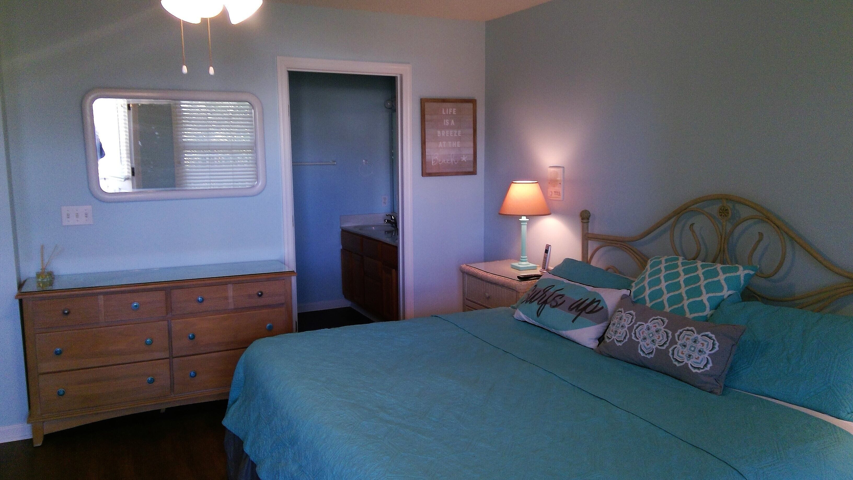 A bedroom with a bed, dresser, nightstand, lamp, and a door leading to a bathroom.