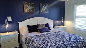 A bedroom with a white headboard, a patterned bedspread, two nightstands with lamps, and two framed wall art pieces. - Gulf View 4/4.5-Seacliffs /dog friendly/community pool/ steps to beach-SPECIALS! (Port St Joe)