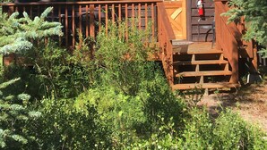A rustic cabin with a wooden deck, a chimney, and a fire extinguisher outside.