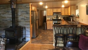 A cozy kitchen with wooden cabinets, a stainless steel refrigerator, a stove, and a stone wall.