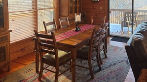 A wooden cabin interior with a dining table, chairs, a ceiling fan, and a view of the outdoors.