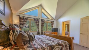 Une chambre à coucher avec un lit, une télévision et de grandes fenêtres avec des rideaux.