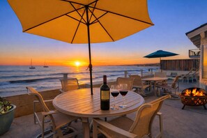 A sunset view from a patio with a table, chairs, a bottle of wine, and a fire pit. - Santa Cruz N At The Beach! Oceanfront w/ Amazing Sunsets! (Santa Cruz)