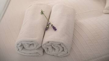 A neatly made bed with two rolled towels and a lavender sprig, a white canopy, and a wooden nightstand with a book.