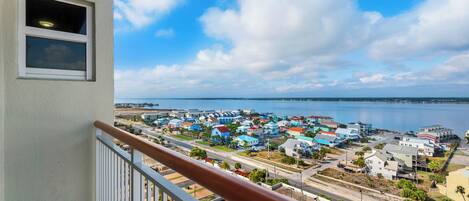 A balcony with a view of a coastal town, featuring a mix of residential and commercial buildings, a clear sky, and a calm sea.