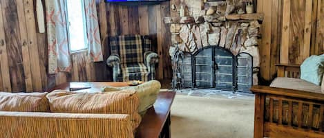 A cozy cabin-style room with a stone fireplace, plaid furniture, and a television displaying a movie poster.