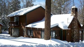 Eine zweistöckige Blockhütte mit Balkon, umgeben von schneebedeckten Bäumen.