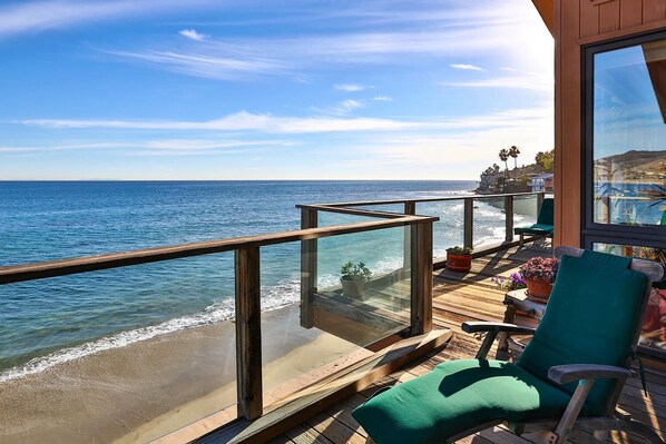 A balcony with a view of the ocean, wooden deck, and green chairs.