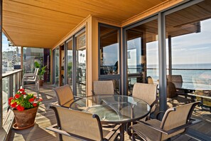 A deck with a glass table and chairs, overlooking a body of water.